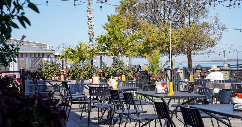 Exterior, patio, black tables, chairs, string lights, and potted plants near a waterfront