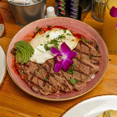 Steak Chilaquiles topped with fried egg, sliced avocado and a flower garnish.