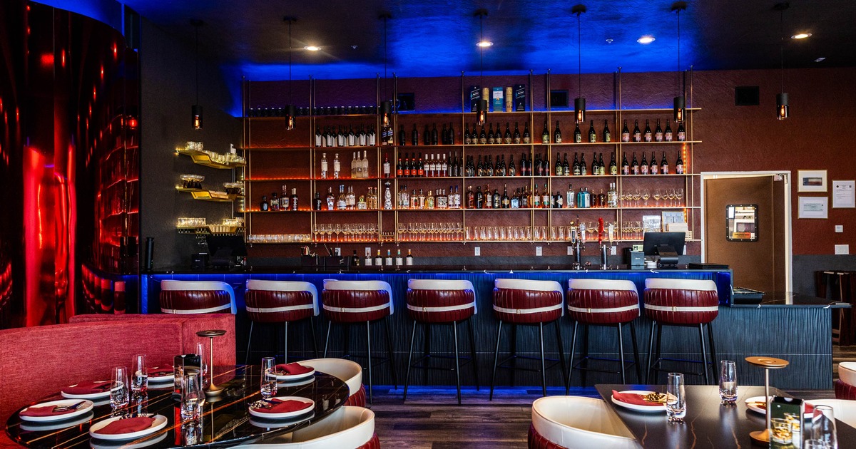 A modern bar - a long counter, red and white stools and shelves stocked with liquor bottles