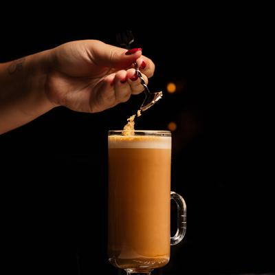 Coffee beverage being prepared by adding brown sugar to the top with a spoon.