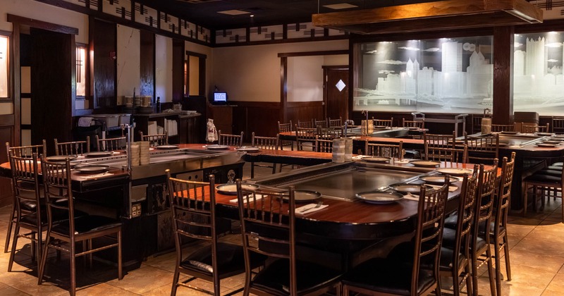 Interior of a restaurant with hibachi tables and wooden chairs