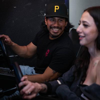 A couple of customers are smiling while playing arcade racing  games.