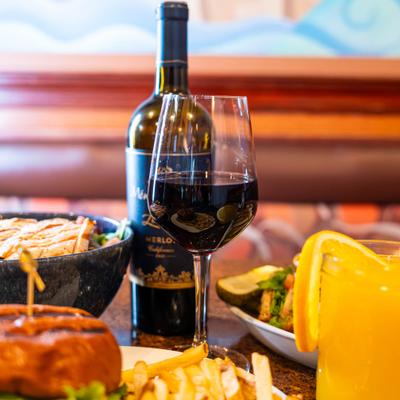 Glass of red winr served on the table with a bottle and various dishes.