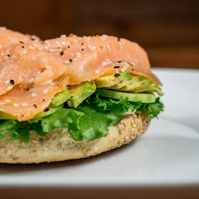 Open faced salmon sandwich featuring avocado, fresh greens and sesame seeds topping.