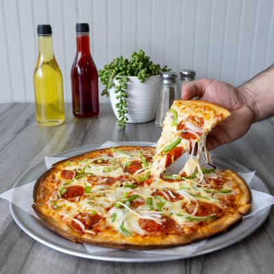 Hand lifting a slice of pepperoni and vegetable pizza from the pie.