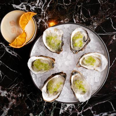 A plate of Half a dozen oysters and a cocktail on a dark marble surface, top down view.