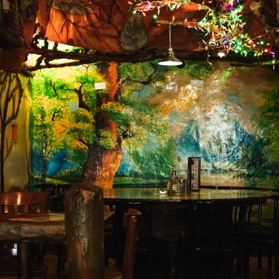 Interior featuring artificial greenery, dim lighting, seating area and a mural of a large tree.