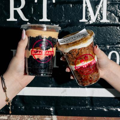 Two cups of cake held inside in front of a brick wall.