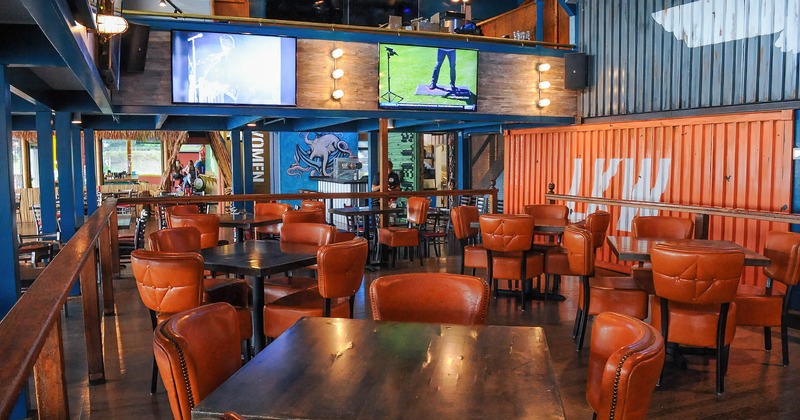Interior, seating area with tables and upholstered leather chairs, TVs on walls
