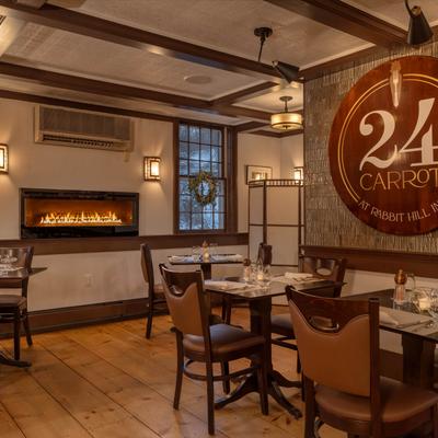 Interior, wooden tables and chairs, a wall-mounted fireplace, and the restaurant's logo on a wall.