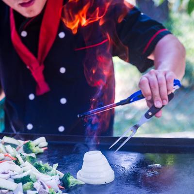 Chef preparing a hibachi onion volcano on a grill.