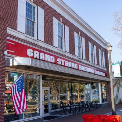 Grand Strand Brewing Company exterior with a brick facade, outdoor seating, and an American flag.