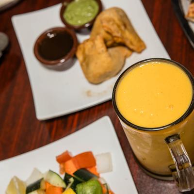 Assortment of food dishes and Mango Lassi served in a beer mug.