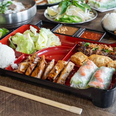 Bento Box with grilled chicken, shrimp summer rolls, fried dumplings, rice and salad.