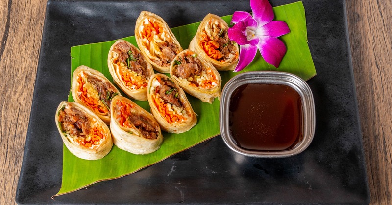 Duck rolls served with a dipping sauce and a purple orchid garnish
