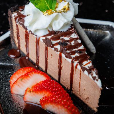 Chocolate mousse cake slice with whipped cream and sliced strawberries.