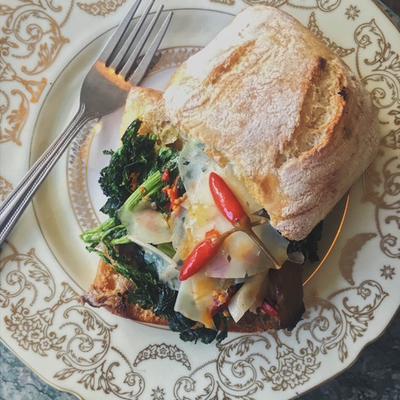 Sandwich with broccoli rabe and cheese, topped with red chili peppers.