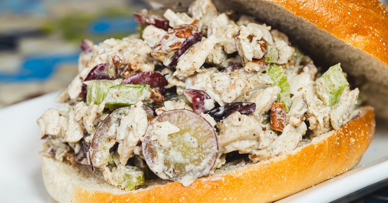 Chicken salad sandwich with grapes and celery on a bun sits on a white plate.