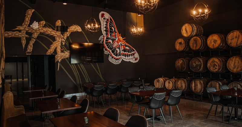 A seating room with mural art on dark walls and barrel racks