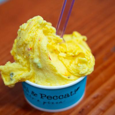 A scoop of saffron vanilla pistachio gelato in a blue cup with a spoon.