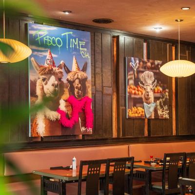 Interior with booths, table, chairs and art prints of llamas hanging on the wall.