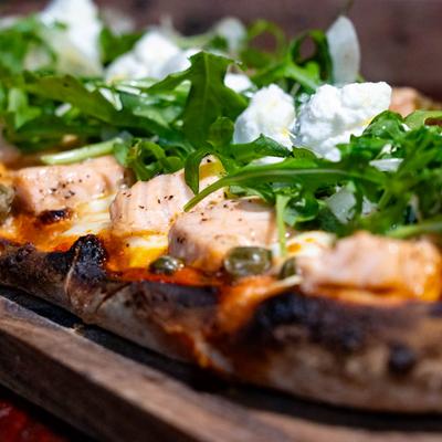 Close up of a pizza topped with salmon, fresh arugula, and cheese.