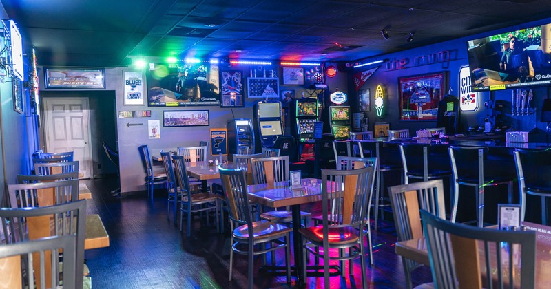 Interior with tables and chairs, neon signs and arcade machines under colorful lighting