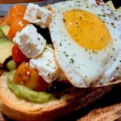Sourdough toast, avocado spread & slices, heirloom tomatoes, feta cheese, sunny egg, drizzled with olive oil..