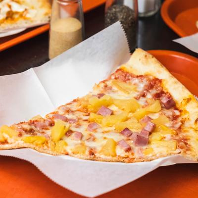 A slice of Hawaiian pizza with ham and pineapple.