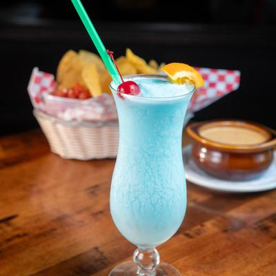 Blue Hawaiian cocktail with food in the background.