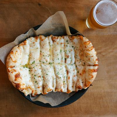 Cheesy breadsticks beside a glass of beer.