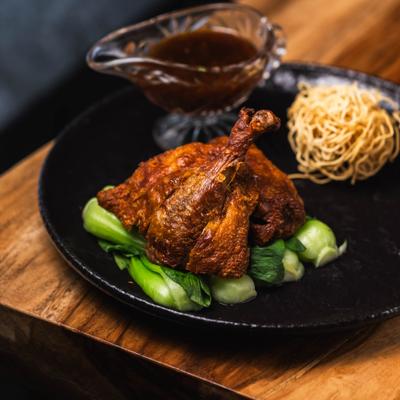 Tamarind Duck served on a bed of bok choy with noodles and a sauce.