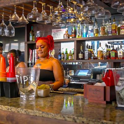 Bar with staff, glasses hung upside down, shelves stocked with liquor bottles.