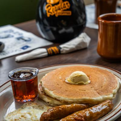 Buttermilk pancakes served with eggs, sausage links, and maple syrup.