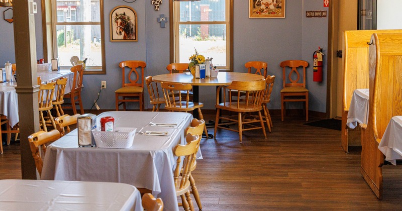 Interior view of a restaurant featuring wooden tables and chairs, white tablecloths
