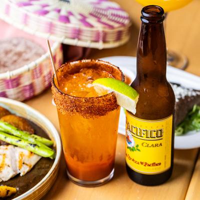 Beer bottle next to a michelada with chili rim and lime.
