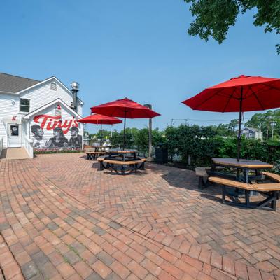 Outdoor patio dining area with picnic tables and red umbrellas on a brick patio.