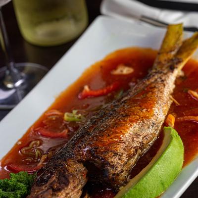 Whole fish in a red sauce with peppers and avocado