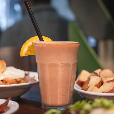 Fresh-squeezed juice garnished with an orange slice, surrounded by plates of food.