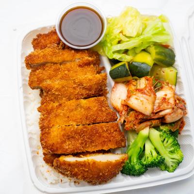 Chicken Katsu  on rice, kimchi, steamed broccoli, cucumber, cabbage, and a brown sauce.