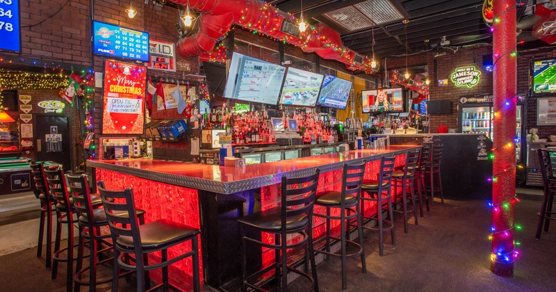 A vibrant sports bar with a glowing bar counter, black chairs, and festive Christmas decorations
