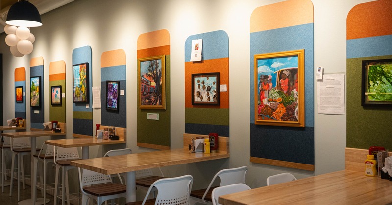 Interior of a cafe with tables and chairs beneath colorful framed artworks on a wall