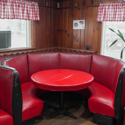 Retro-style diner booth - red vinyl seating, matching round table; wooden walls; checkered curtains.