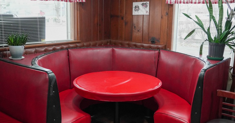 Retro-style diner booth - red vinyl seating, matching round table; wooden walls; checkered curtains