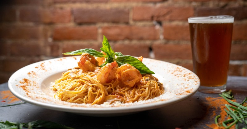 Shrimp pasta topped with fresh basil and a glass of beer, brick wall background