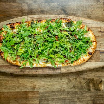 Grilled Flat Bread topped with fresh arugula and served on a rustic wooden board.