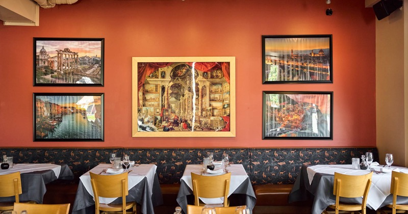Interior, banquette seating with set tables by a wall decorated with pictures