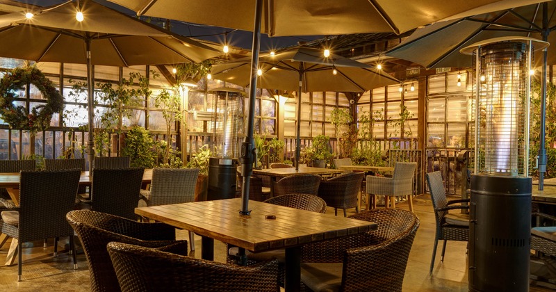Exterior, seating area, wooden top tables with wicker chairs, parasols, space heaters