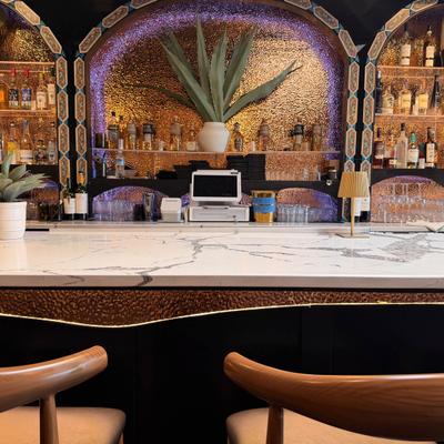 Upscale Latin fusion bar featuring elegant marble counters and illuminated textured copper arches.