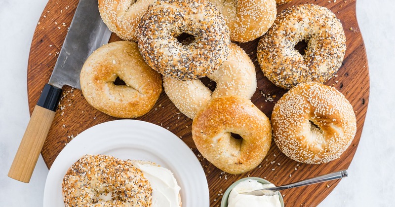Assorted bagels on a wooden board with cream cheese and a knife